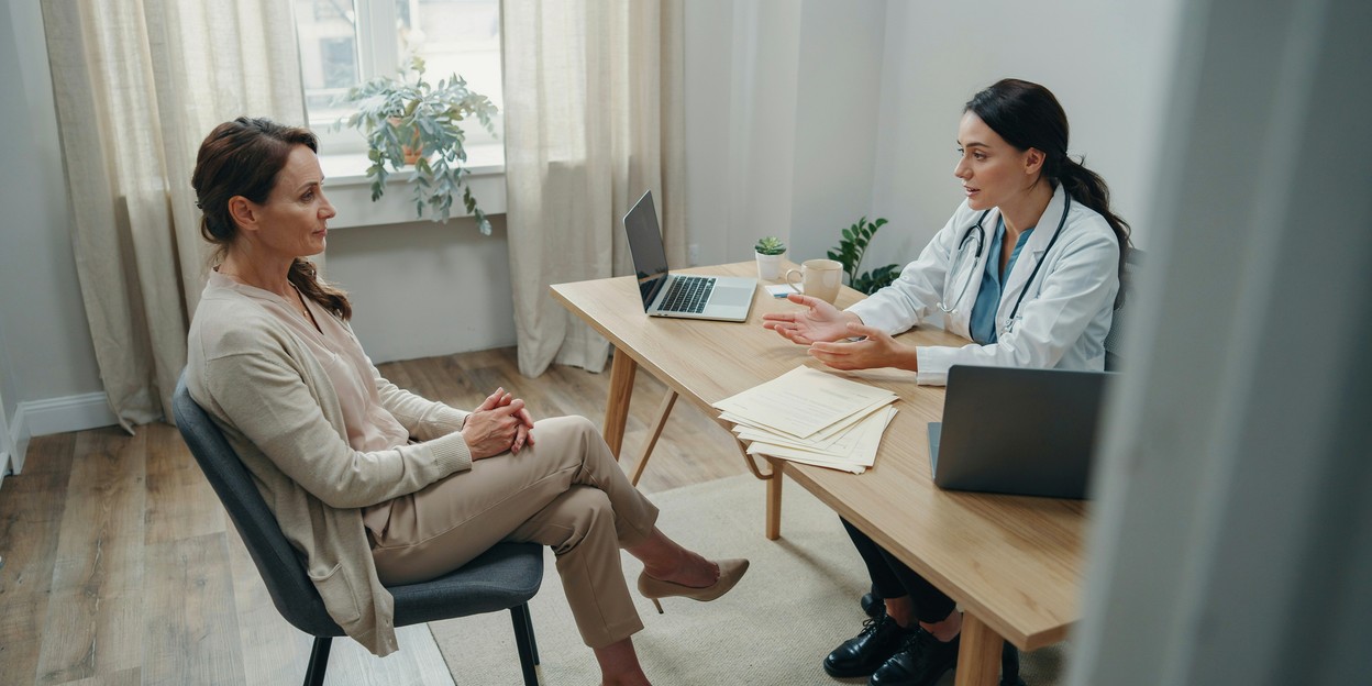 Woman in her fifties talking with her GP across a desk in a bright consulting room