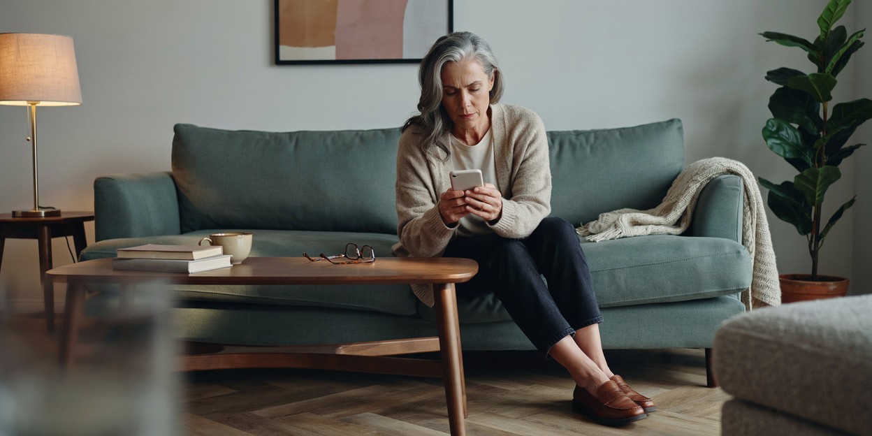 Woman in her fifties reading on her phone while sitting on a sofa in evening lamplight