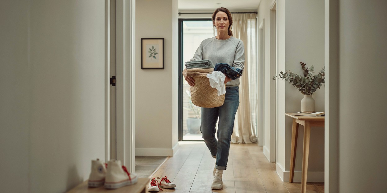 Woman in her forties carrying a full laundry basket along a hallway at home