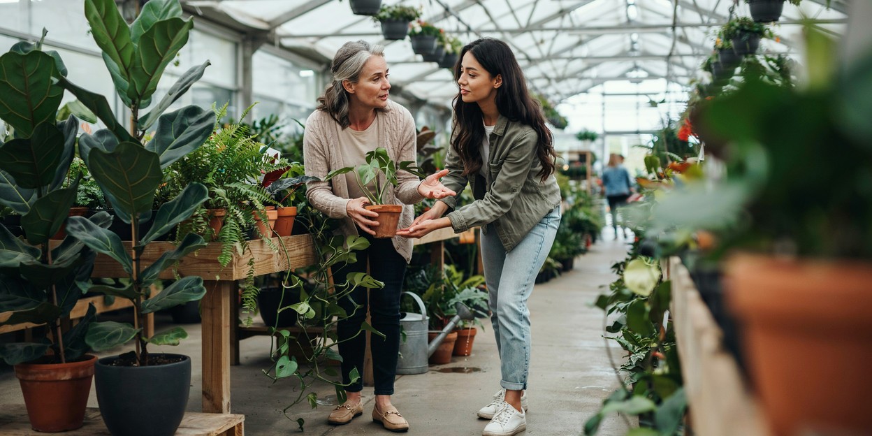 Woman in her fifties and her adult daughter looking at potted plants together in a garden centre
